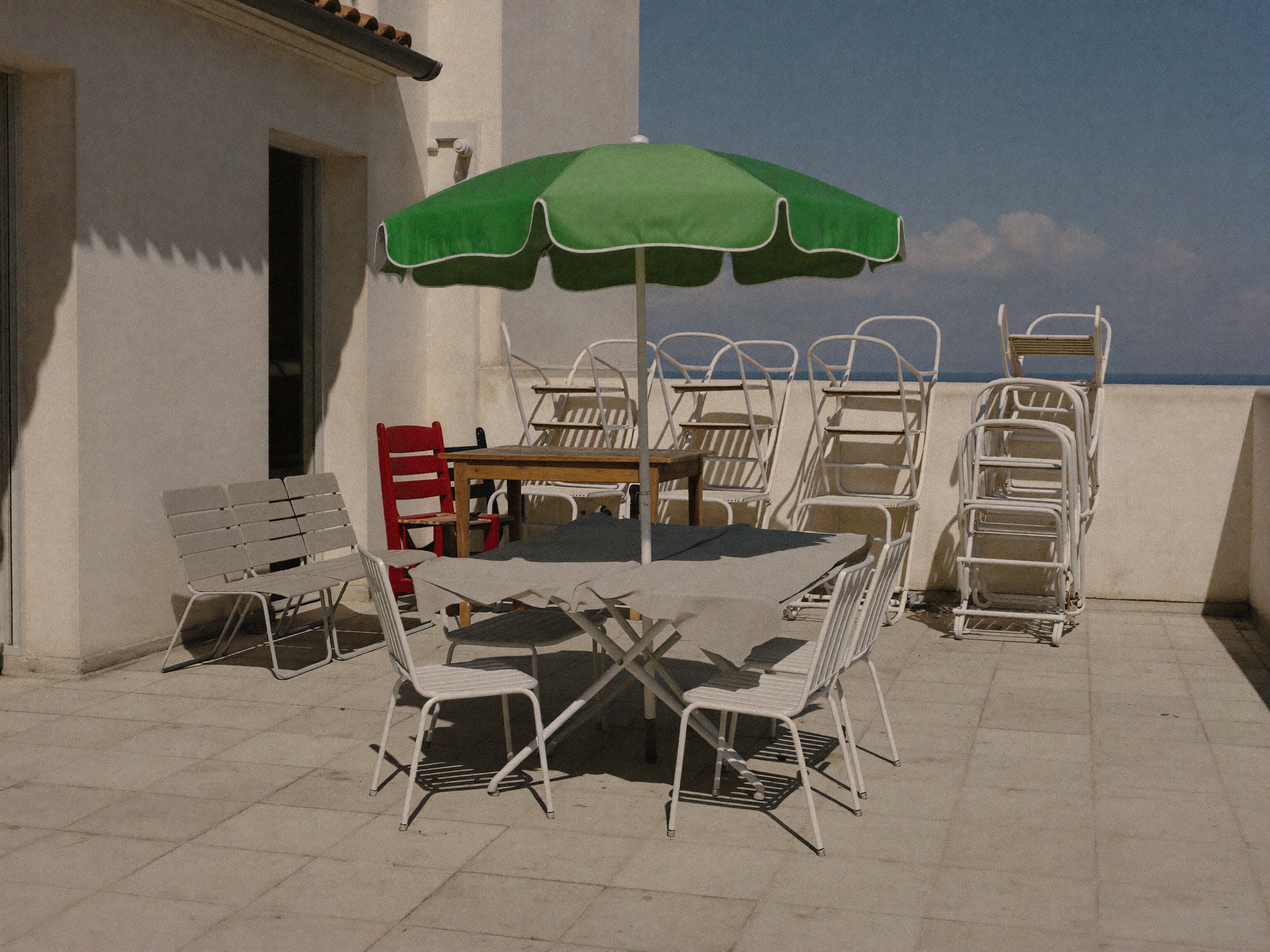 Leere Terrasse mit zusammengelegtem Sonnenschirm und gestapelten Gartenmöbeln