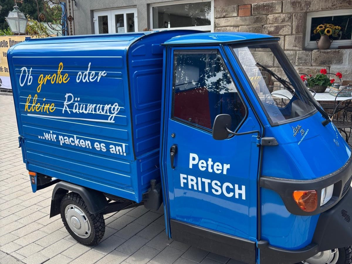 Blaue Piaggio Ape von Peter Fritsch mit der Aufschrift Ob große oder kleine Räumung - wir packen es an