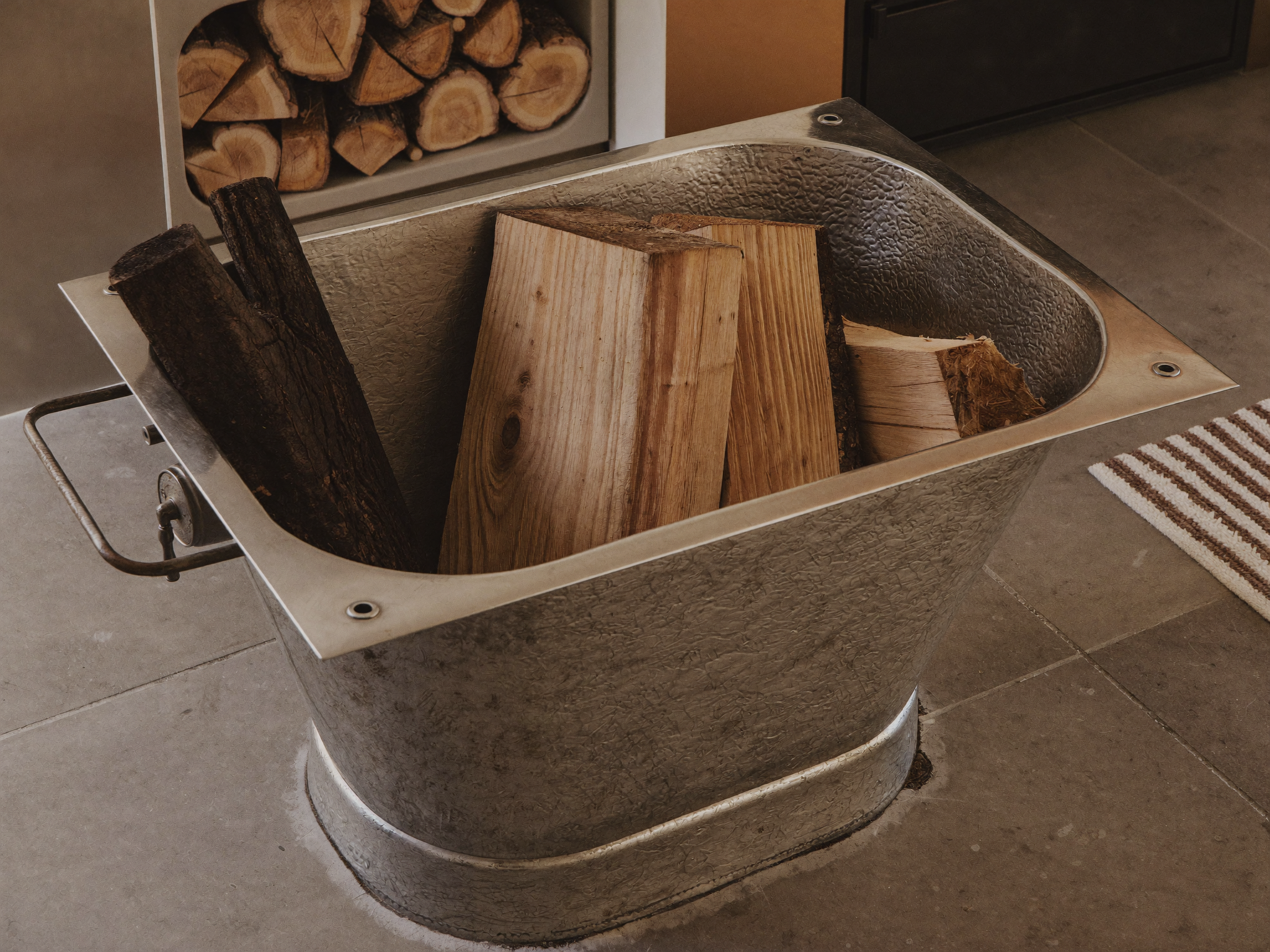 Zinkwanne mit Brennholz neben einem Kamin